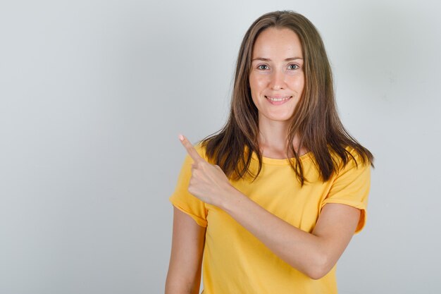 Young woman pointing finger backwards in yellow t-shirt and looking cheerful