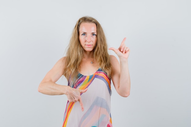 Free photo young woman pointing fingers up and down in summer dress and looking sensible