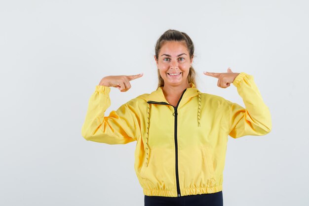 Young woman pointing at her smile in yellow raincoat