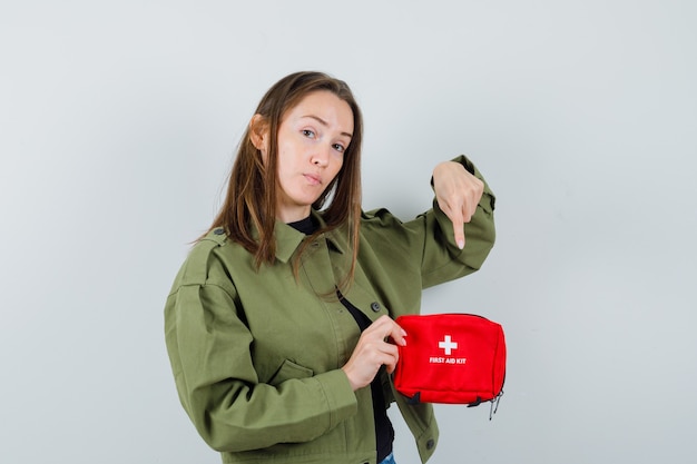 Free photo young woman pointing to inside of first aid kit in green jacket , front view.