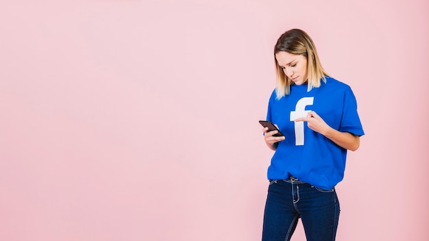 Young woman pointing at mobile phone over pink background