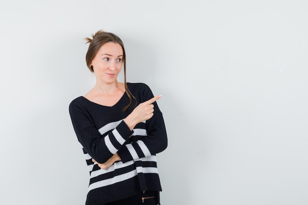 Young woman pointing right with index finger in black blouse and black pants and looking happy