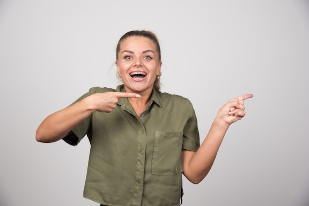 Young woman pointing at something on gray wall.