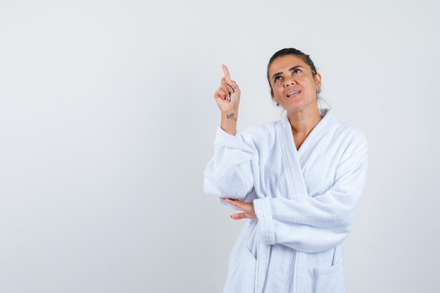 Young woman pointing up in bathrobe and looking confident