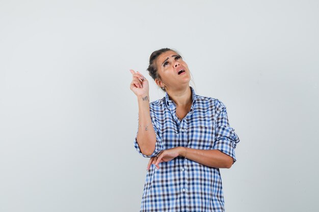 Young woman pointing up in checkered shirt and looking concentrated.