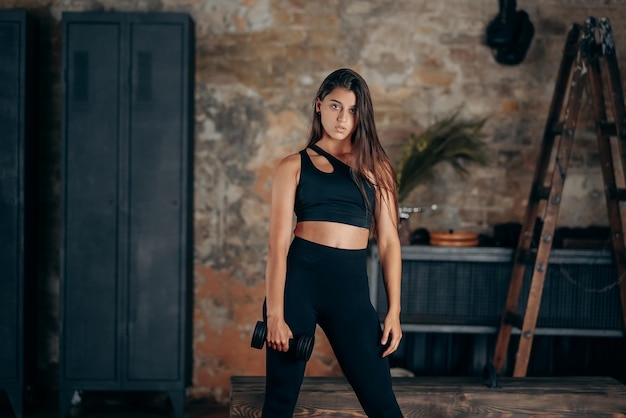 Young woman posing at the camera with dumbbells in her hands