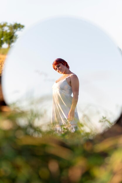 Young woman posing confidently outdoors using a round mirror