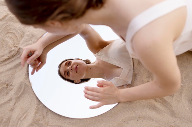 Young woman posing outdoors on a beach using a round mirror