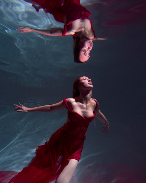 Young woman posing submerged underwater in a flowy dress