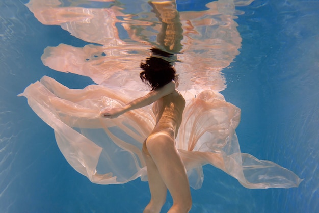 Young woman posing submerged underwater in a flowy dress