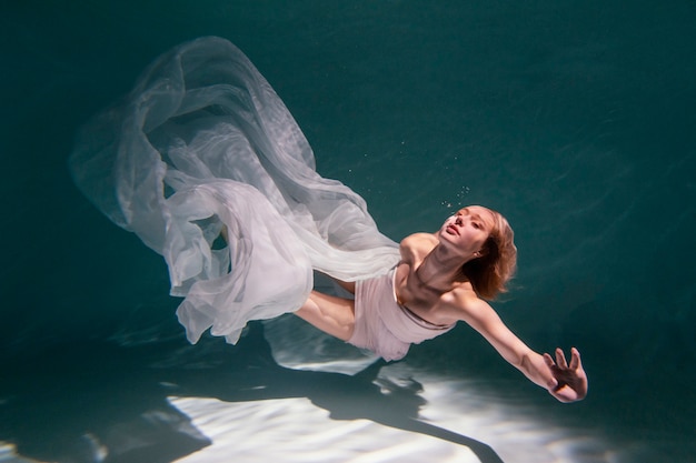 Young woman posing submerged underwater in a flowy dress