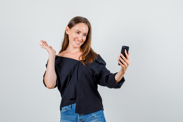 Young woman posing while taking selfie on smartphone in shirt, shorts and looking cute. front view.