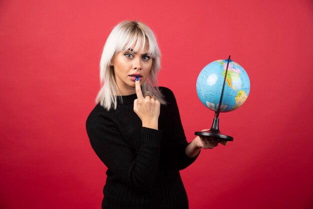 Young woman posing with a globe on a red background. High quality photo