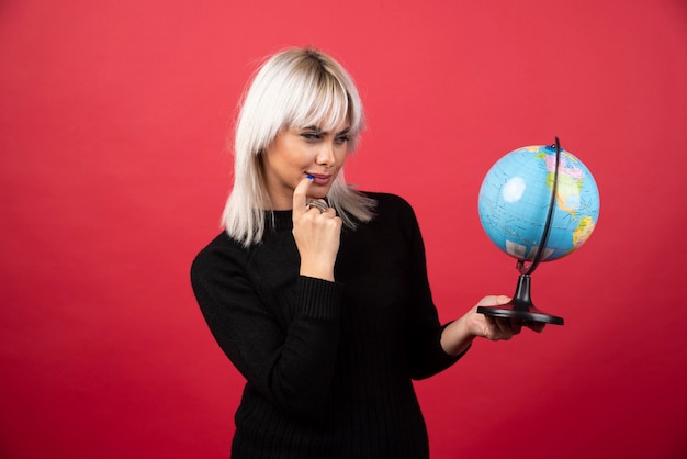 Young woman posing with a globe on a red background. High quality photo