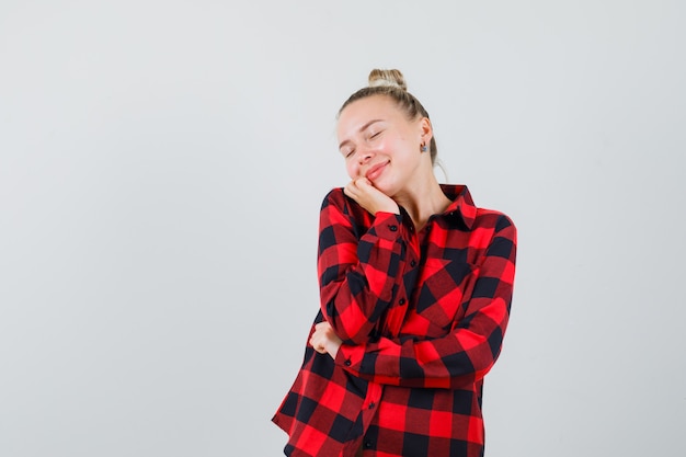 Young woman posing with hand on chin in checked shirt and looking peaceful