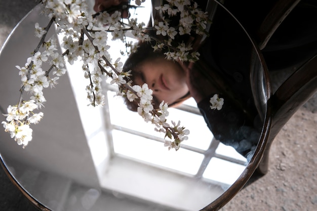 Young woman posing with mirror on chair and flower