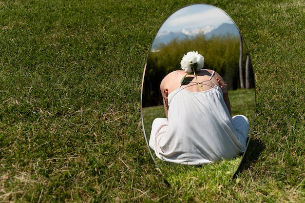 Free photo young woman posing with peony flower in the mirror on the grass outdoors