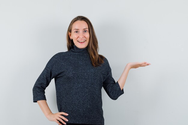 Young woman pretending to hold or show something in shirt and looking happy. front view.