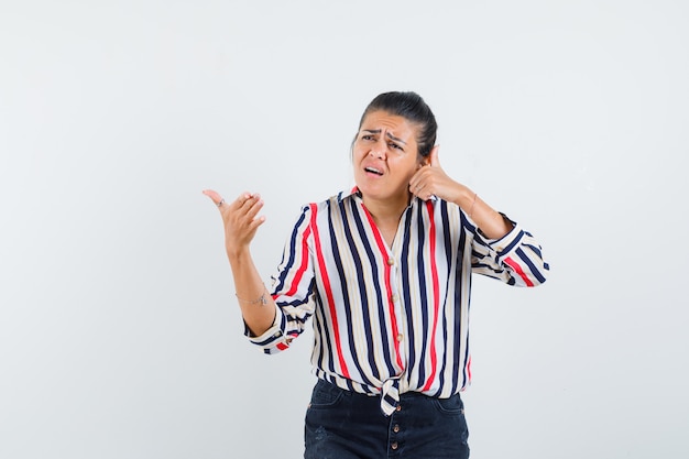 Young woman pretending like talking on phone in striped blouse and looking curious.