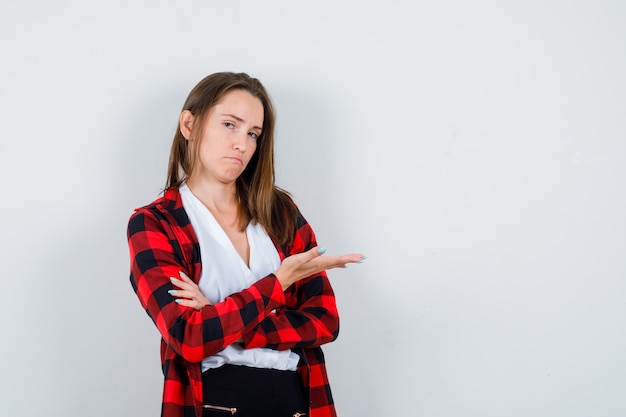 Young woman pretending to show something in casual clothes and looking reluctant , front view.