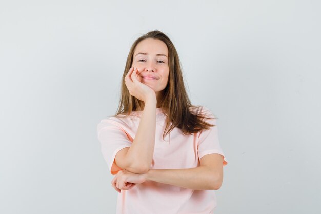 Young woman propping chin on palm in pink t-shirt and looking cheery.