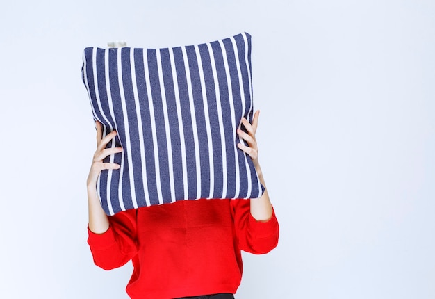 Free photo young woman putting a blue striped pillow to her face.