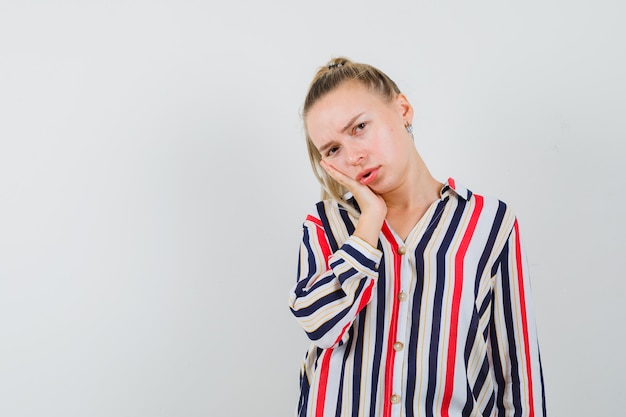 Young woman putting her hand on cheek in striped blouse and looking doubtful