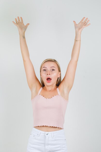 Young woman raising arms in singlet, mini skirt and looking happy.