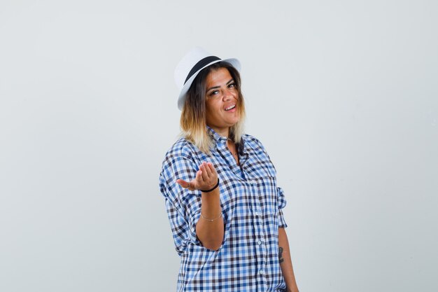 Young woman raising hand with open palm in checkered shirt and looking focused.