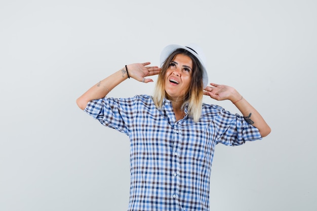 Free Photo young woman raising hands to defend in checkered shirt and looking troubled.