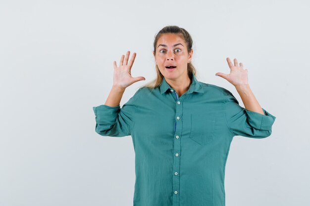 Young woman raising hands for defending in blue shirt and looking anxious