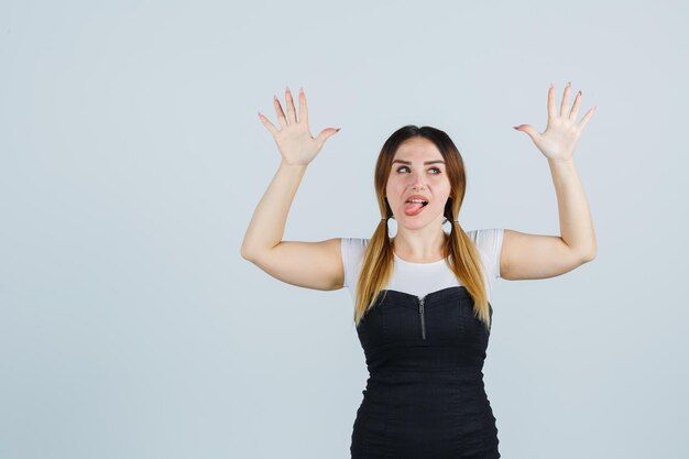 Young woman raising hands over head while sticking out tongue