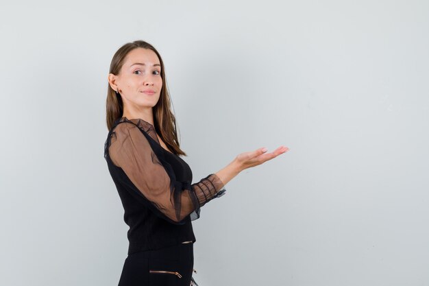 Young woman raising her hand with open palm showing something in black blouse and looking focused . space for text