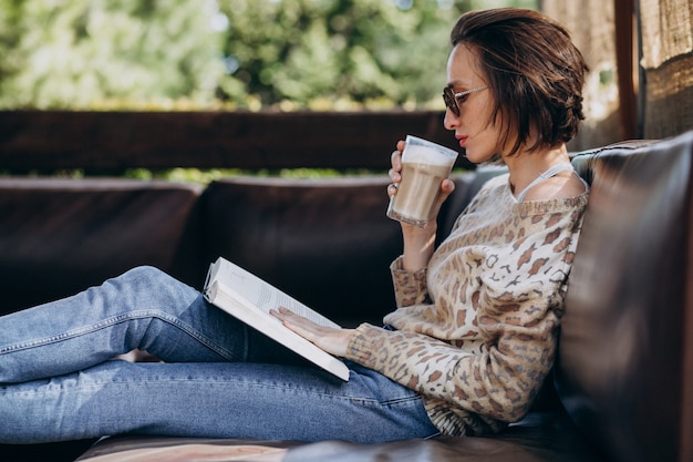 Free photo young woman reading book and drinking coffee