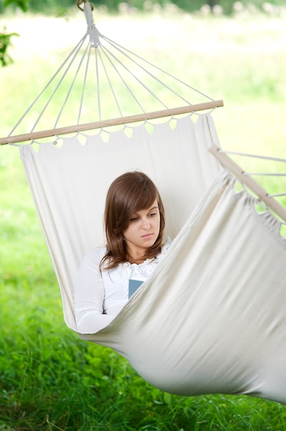 Free photo young woman reading a book in hammock