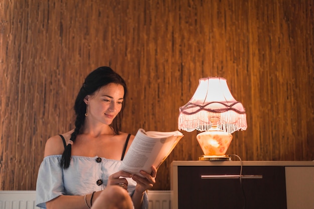 Young woman reading book near the illuminated light lamp