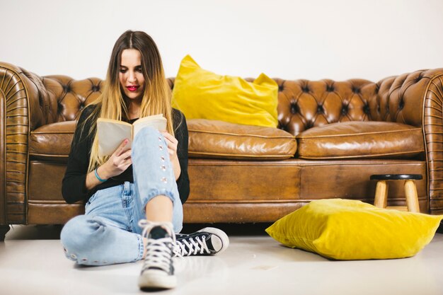 Young woman reading book near sofa