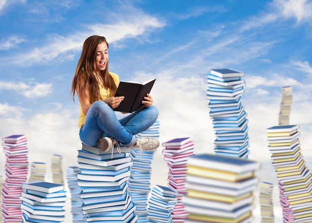 young woman reading a book sitting on a books pile on the sky