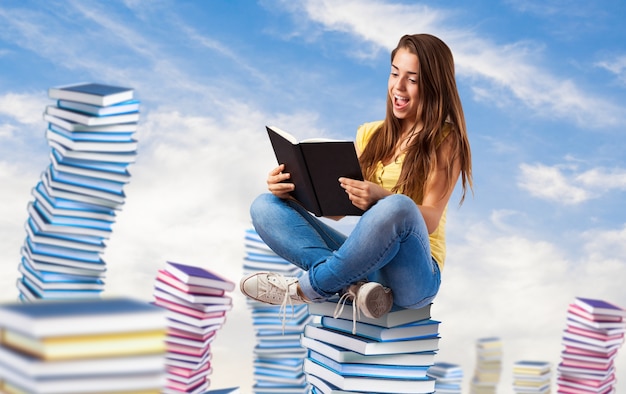 young woman reading a book sitting on a books pile on the sky