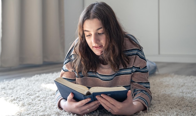 A young woman reading a book while lying on the floor at home