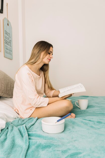 Young woman reading during breakfast on bed