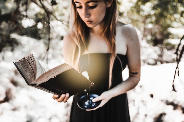 Free photo young woman reading old book with candle in woods