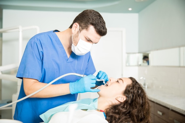 Young woman receiving dental treatment from male dentist in clinic