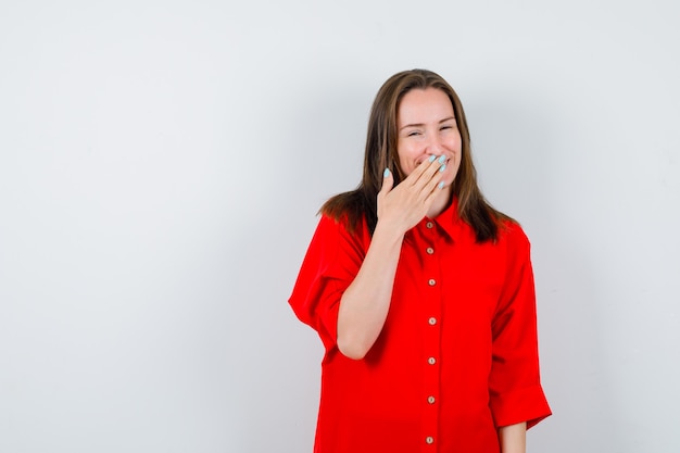 Free photo young woman in red blouse keeping hand on mouth and looking merry , front view.