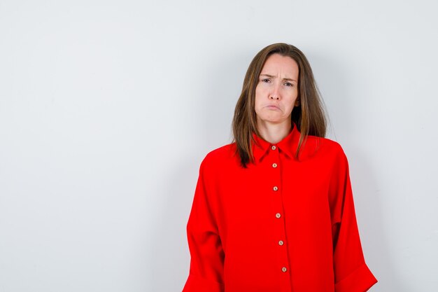 Young woman in red blouse looking with frowning face, curving lower lip and looking dismal , front view.