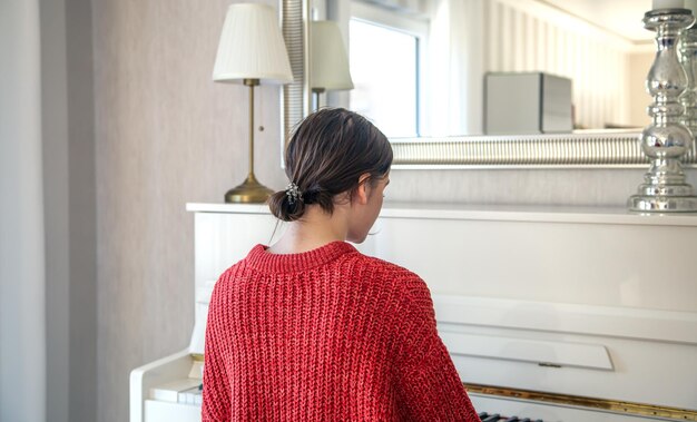 A young woman in a red knitted sweater near a white piano