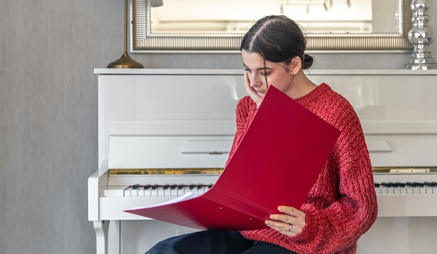 Free photo a young woman in a red knitted sweater near a white piano