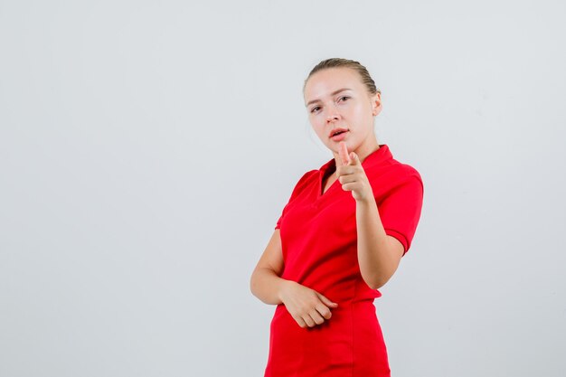 Young woman in red t-shirt pointing and looking confident