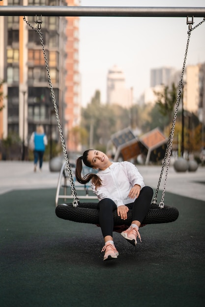 Young woman rides on a swing at the playground.