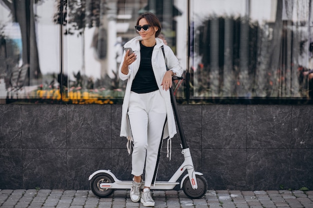 Young woman riding scotter in town and using phone